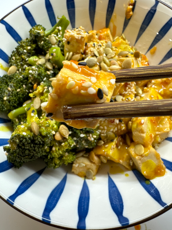 Chopsticks holding Sticky Tofu topped with sesame seeds