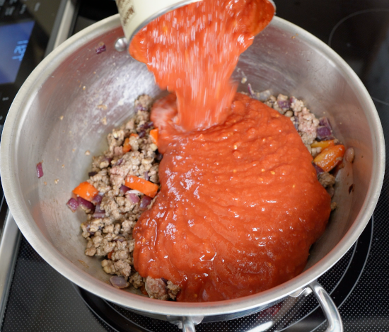 Crushed tomatoes being added to the dish