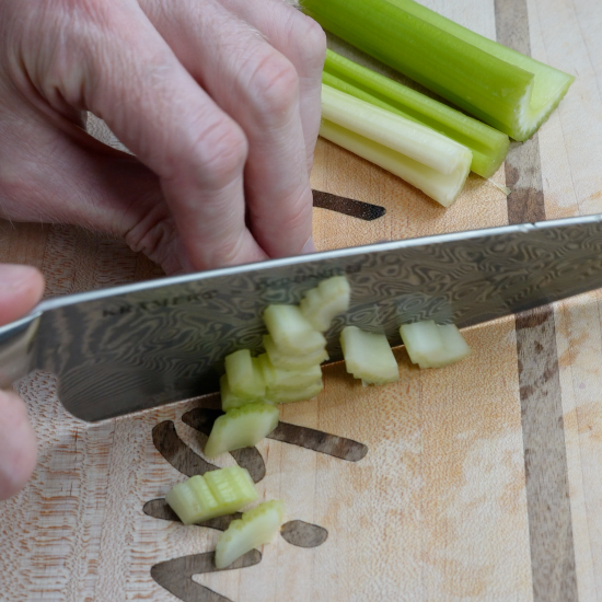Chopped celery with a sharp knife on a cutting board. 