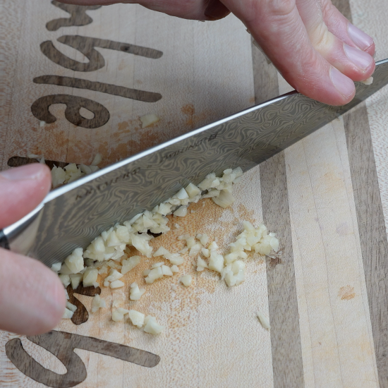 Mincing garlic with a sharp knife on a cutting board. 
