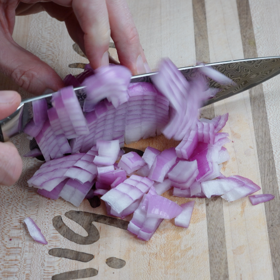 Chopping red onion with a sharp knife on a cutting board. 