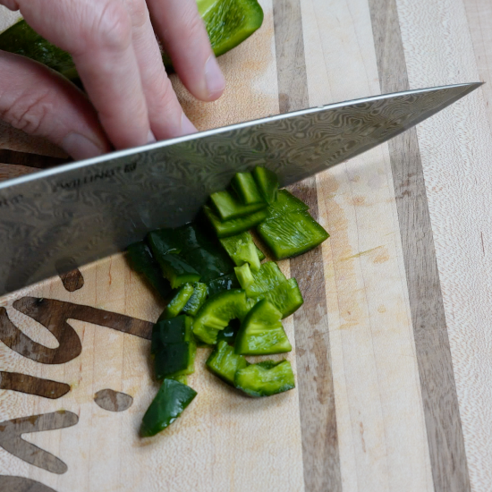 Dicing poblano with a sharp knife on a cutting board. 